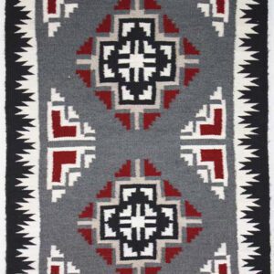 Geometric patterned textile with red, black, and white motifs on gray.