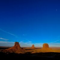 Sunlit desert landscape with towering rock formations under a deep blue sky.